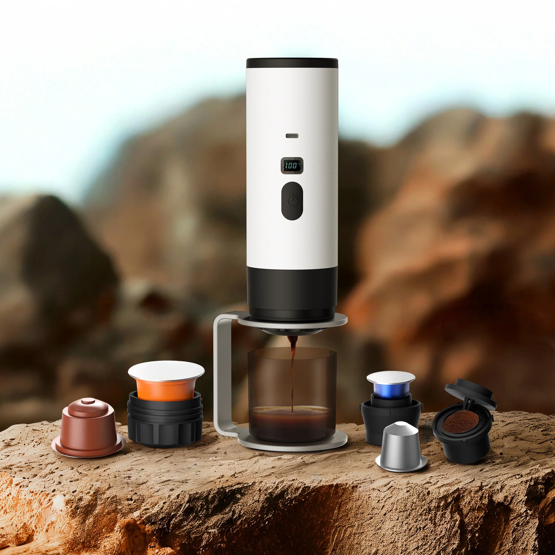 Portable coffee maker brewing espresso outdoors with assorted pods on a rocky surface