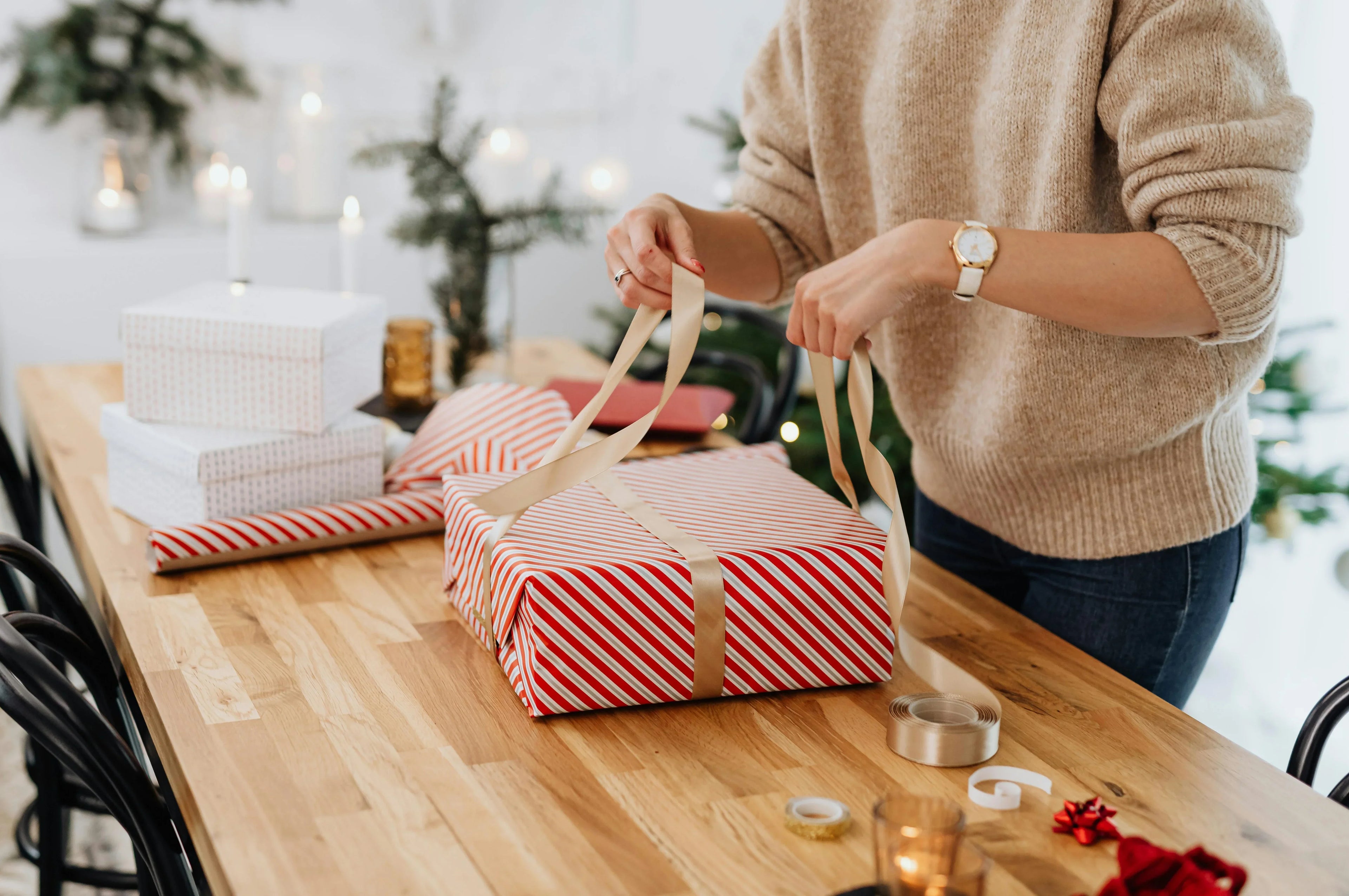Person wrapping striped gift boxes with ribbon on festive wooden table