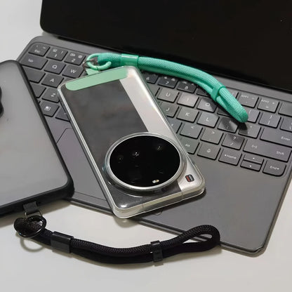 Transparent phone case with green strap on laptop keyboard, nearby black phone case
